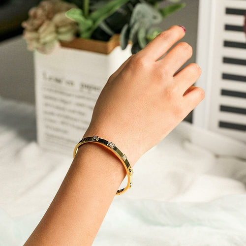 Hand wearing a gold bracelet with a blurred indoor background